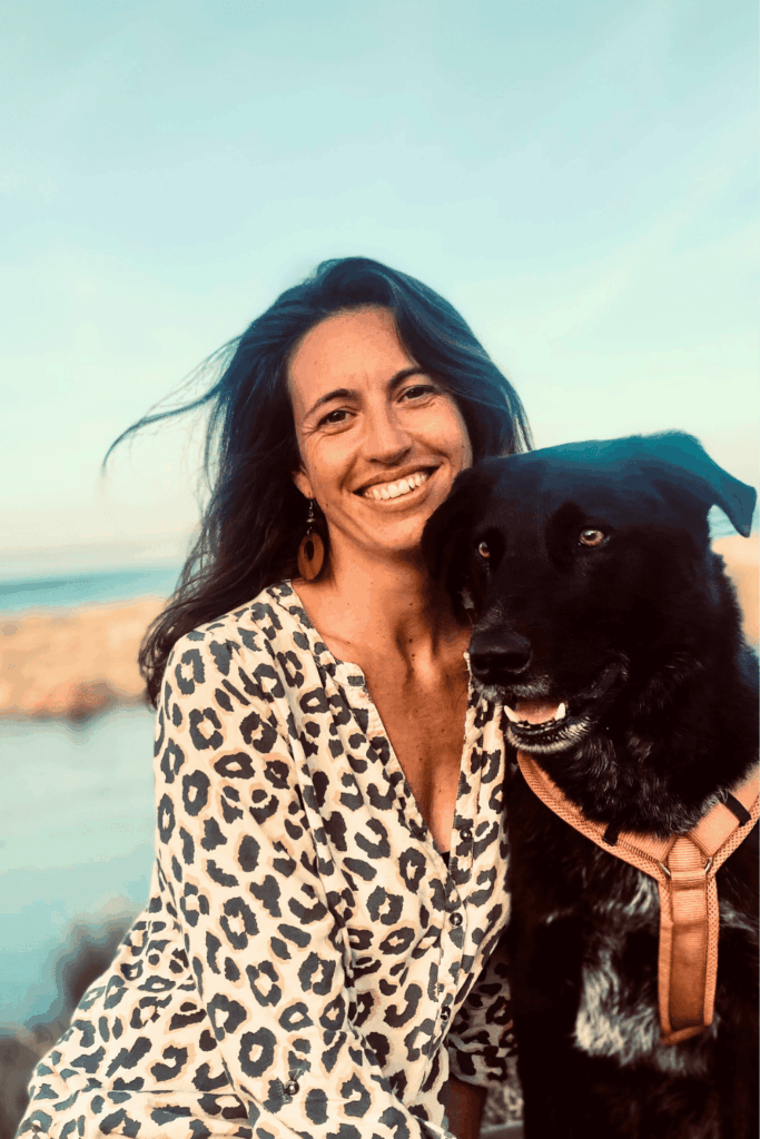 Eine Frau sitzt neben Ihrem großen schwarzen Hund und lächelt in die Kamera