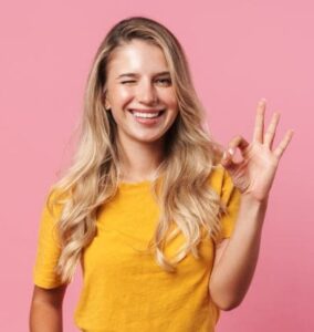 Eine blonde Frau zwinkert und zeigt ein OK -Zeichen mit dem Daumen und Zeigefinger